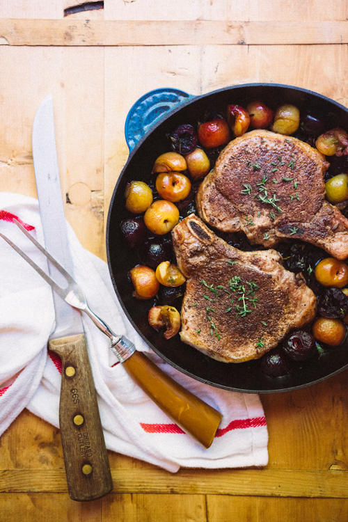 pan with pork chops sprinkled with herbs, surrounded by balsamic cherries